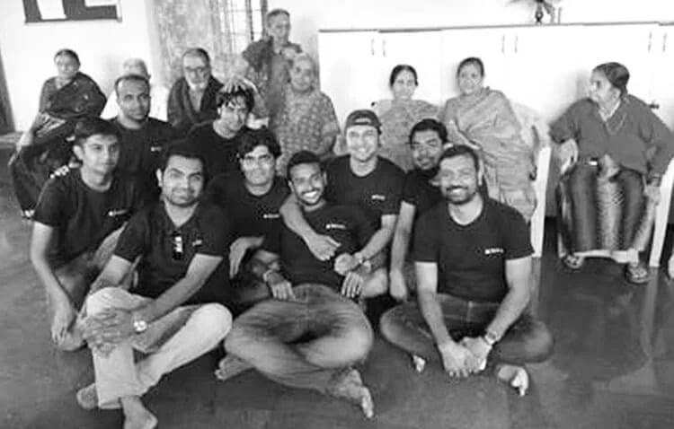 A gathering of Tricon employees sitting on floor, while elderly women sitting on chairs at the back. They are happily posing for a picture