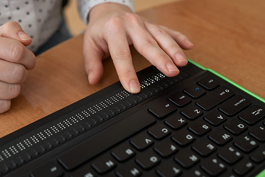 A hand using a computer keyboard with a Braille input